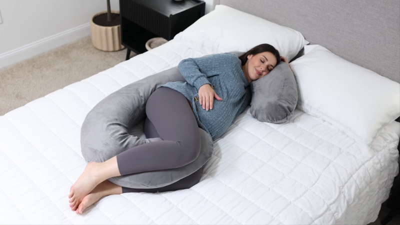 Trudnica leži na boku uz sivi jastuk za trudnice